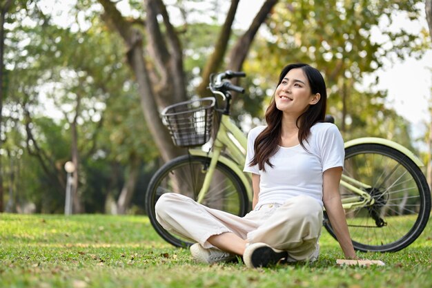 La donna asiatica felice e spensierata si siede sull'erba guardando la splendida vista della natura