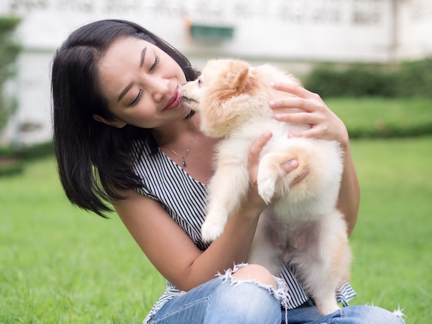 La donna asiatica gioca con il suo cucciolo pomeranian nel giardino.