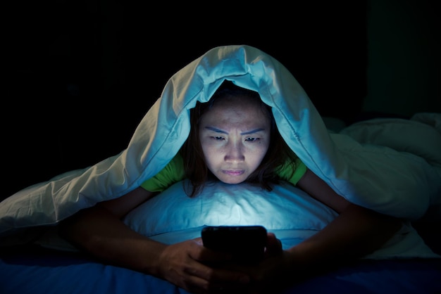 La donna asiatica gioca con lo smartphone nel letto di notte. Persone della Thailandia. Dipendenti dai social media. Gioca a Internet tutta la notte