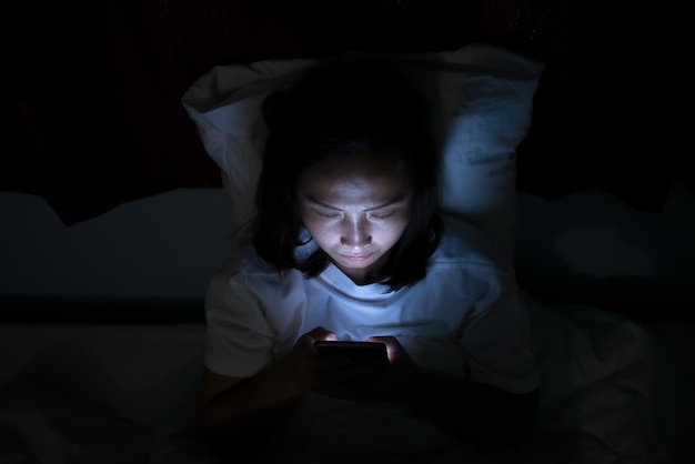 La donna asiatica gioca con lo smartphone nel letto di notteLa gente della Thailandia