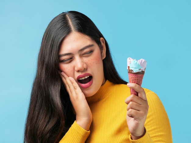 La donna asiatica ha ferito i suoi denti con icacream su fondo blu