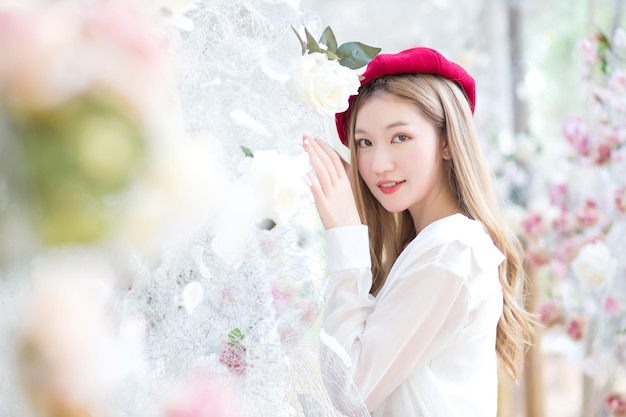 La donna asiatica ha lunghi capelli color bronzo e indossa un abito bianco con berretto rosso mentre si trova in mezzo al giardino fiorito
