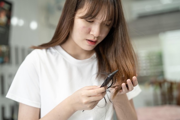 La donna asiatica ha problemi con la caduta dei capelli lunghi attaccata alla spazzola del pettine