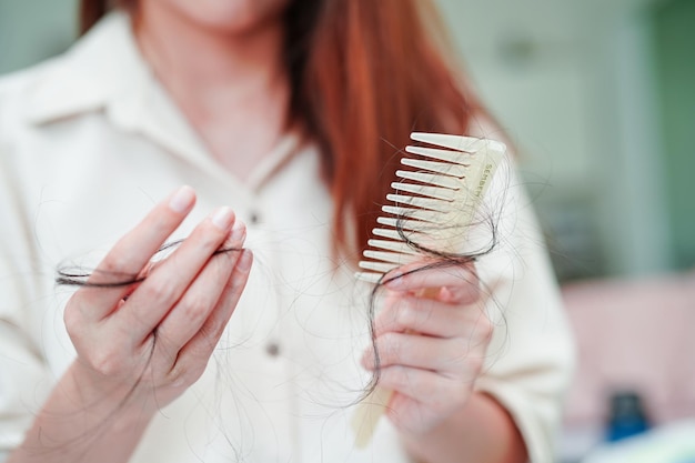 La donna asiatica ha problemi con la caduta dei capelli lunghi attaccata alla spazzola del pettine