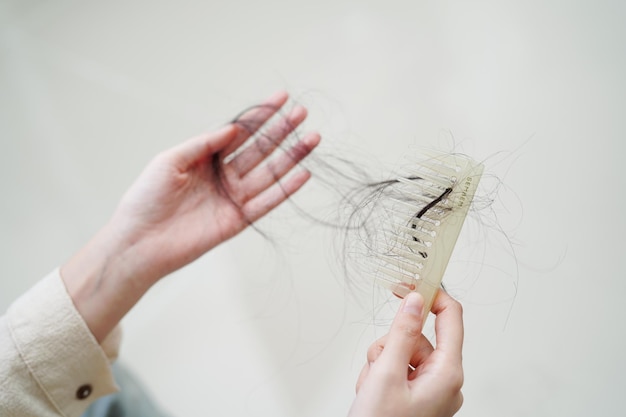 La donna asiatica ha problemi con la caduta dei capelli lunghi attaccata alla spazzola del pettine