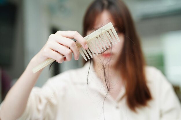 La donna asiatica ha problemi con la caduta dei capelli lunghi attaccata alla spazzola del pettine