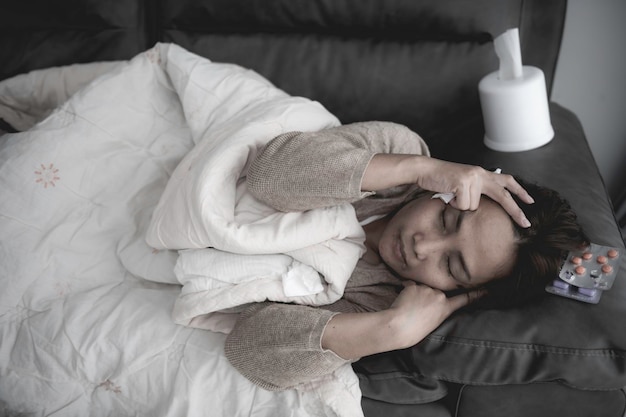La donna asiatica malata si siede sul divano resta a casa La donna si sentiva male e voleva sdraiarsi e riposarsi la febbre alta