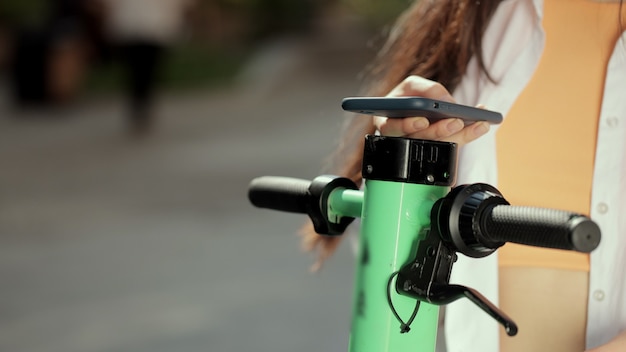 La donna asiatica ravvicinata noleggia uno scooter elettrico utilizzando l'app per telefoni cellulari, un nuovo progetto di condivisione aziendale avviato nel trasporto ecologico della città city