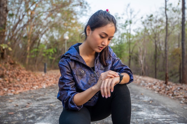 La donna asiatica sta premendo il suo smartwatch per fare jogging al parco