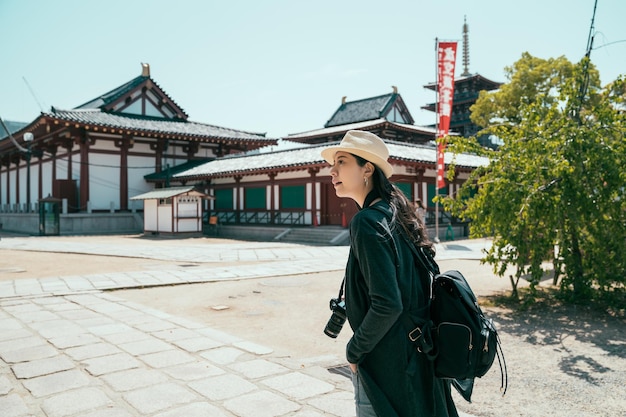 La donna asiatica viaggia da sola in Giappone durante le vacanze estive. zaino in spalla ragazza che cammina nel bellissimo tempio durante una calda giornata di sole con cielo blu. turista femminile porta la macchina fotografica durante la visita nel santuario di shitennoji