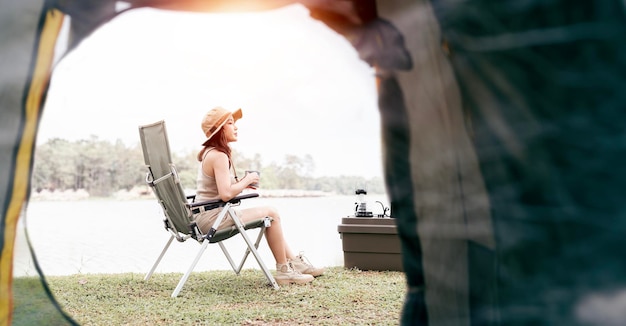 La donna asiatica viaggia e si accampa da sola seduta sulla sedia vicino al lago