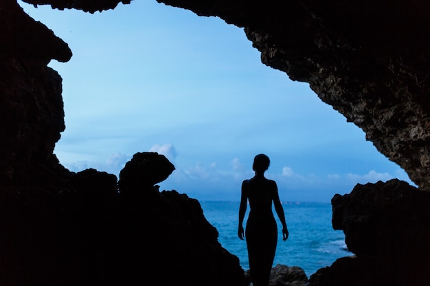 La donna aspetta il tramonto nella grotta balinesse sulla spiaggia dell'oceano,