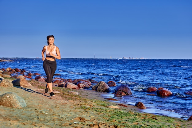 La donna attiva in abbigliamento sportivo corre vicino alla riva