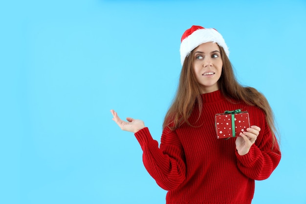 La donna attraente con il cappello di Babbo Natale tiene una scatola regalo su sfondo blu