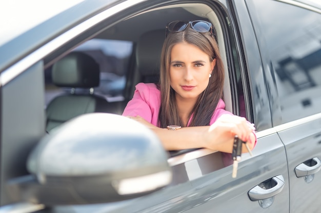 La donna attraente distribuisce la chiave dell'automobile della tenuta dell'automobile della finestra.