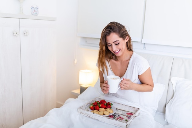 La donna attraente felice si è svegliata la mattina a letto. Buongiorno e colazione fresca e bella per la ragazza