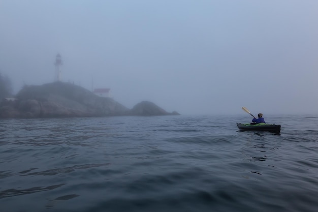 La donna avventurosa è in kayak di mare vicino a un faro durante un tramonto invernale vibrante e nebbioso