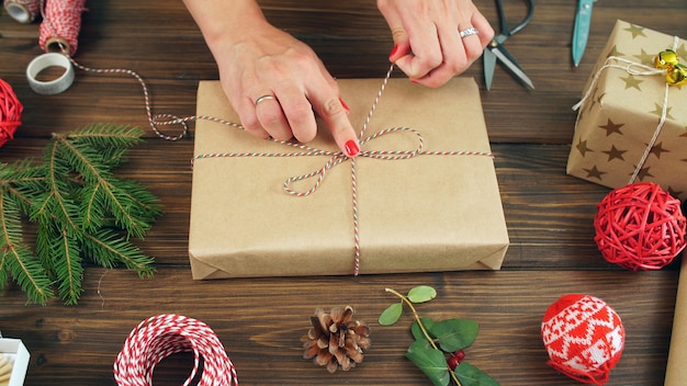 La donna avvolge i regali mentre si prepara per il Natale. Primo piano delle mani di una donna e un regalo