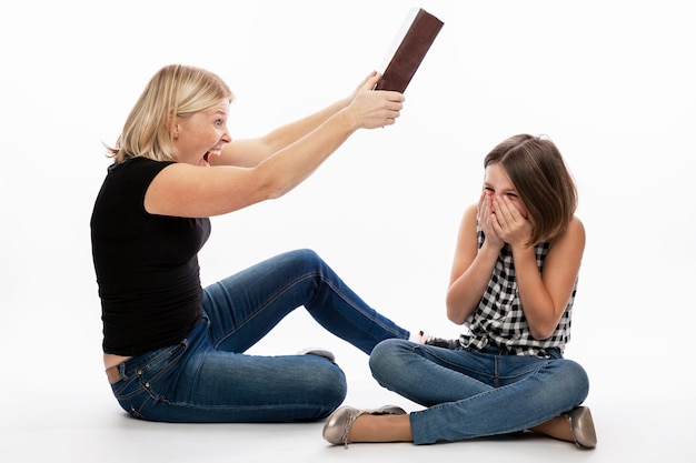 La donna batte la figlia dell'adolescente con un libro pesante. Rapporti familiari e difficoltà dell'apprendimento a distanza durante il periodo di isolamento. Muro bianco.