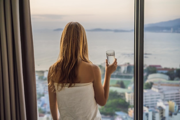 La donna beve acqua al mattino sullo sfondo di una finestra con vista sul mare
