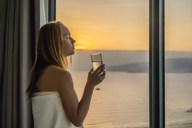 La donna beve acqua al mattino sullo sfondo di una finestra con vista sul mare