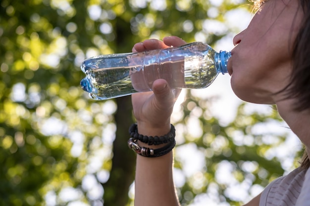 La donna beve acqua potabile fresca da una bottiglia di plastica in una giornata calda