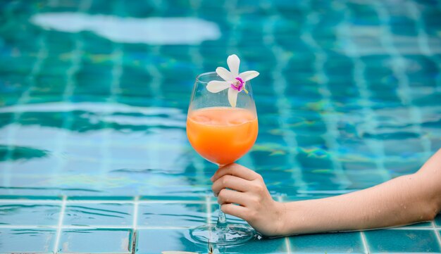 La donna beve un bicchiere da cocktail di succo d'arancia in piscina. Vacanze estive e relax da soli a casa.