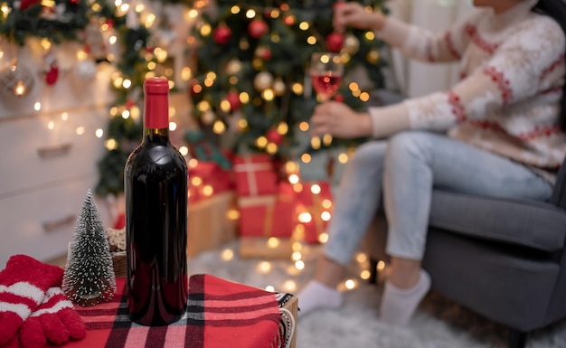 La donna beve vino rosso e decora l'albero di Natale per la festa di Natale e Capodanno a casa.