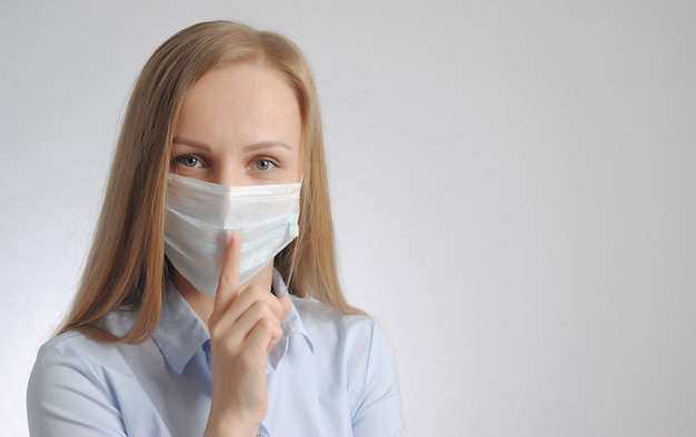 La donna bionda con la mascherina medica mostra il silenzio e sii gesto calmo