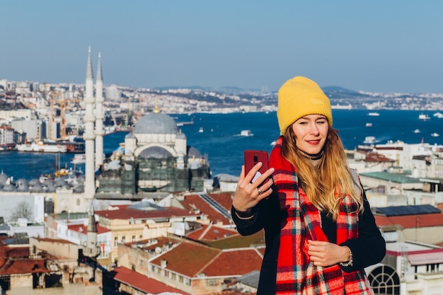 La donna bionda fa foto al telefono sul tetto del Grand Bazaar, Istanbul, Turchia. La ragazza in un cappello giallo prende un selfie un giorno soleggiato di autunno. La ragazza del viaggiatore cammina attraverso l'inverno Istanbul.