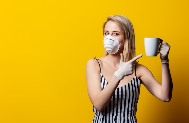 La donna bionda in maschera e guanti tiene la tazza di caffè