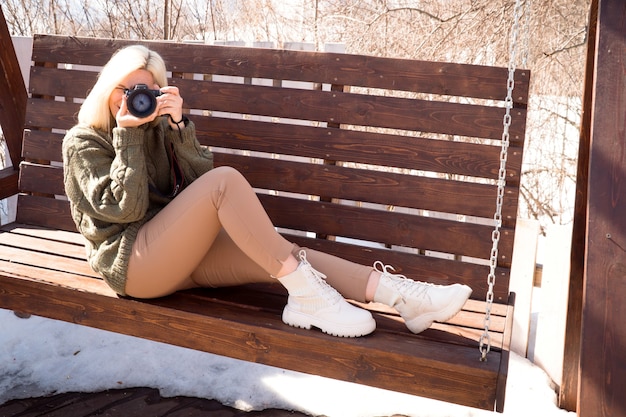 La donna bionda scatta una foto sul canone della fotocamera digitale seduto sul ramo nella soleggiata giornata invernale