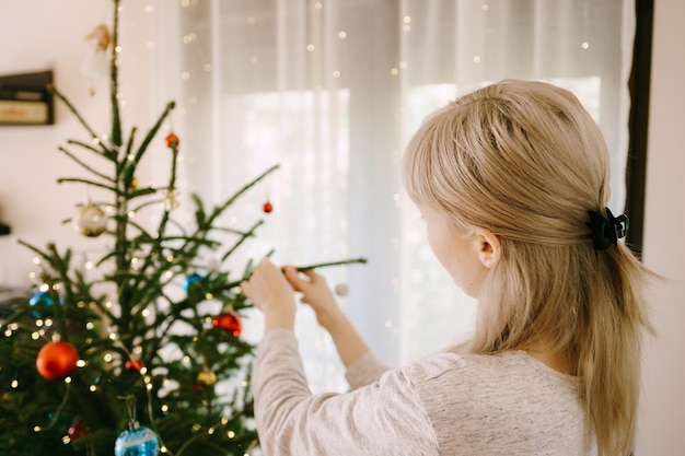 La donna bionda sta decorando l'albero di Natale a casa.