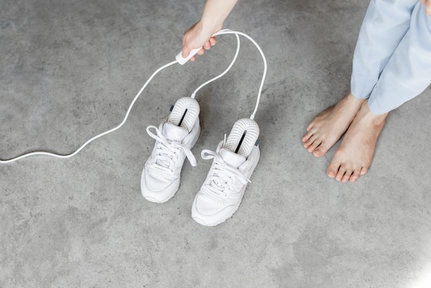 La donna cambia l'asciugascarpe elettrico che asciuga le sue scarpe da ginnastica bianche