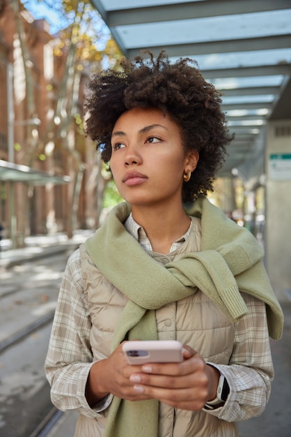 la donna cammina durante il tempo libero in ambiente urbano tiene il telefono cellulare gode della comunicazione dello smartphone con un amico in pose di chat online all'esterno