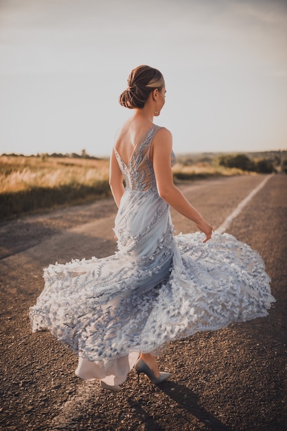 La donna cammina lungo una strada asfaltata in abito lungo al tramonto