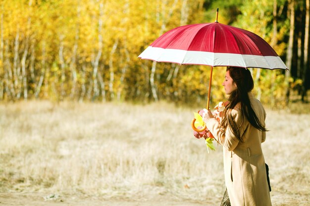 La donna cammina nella foresta d'autunno con l'ombrello