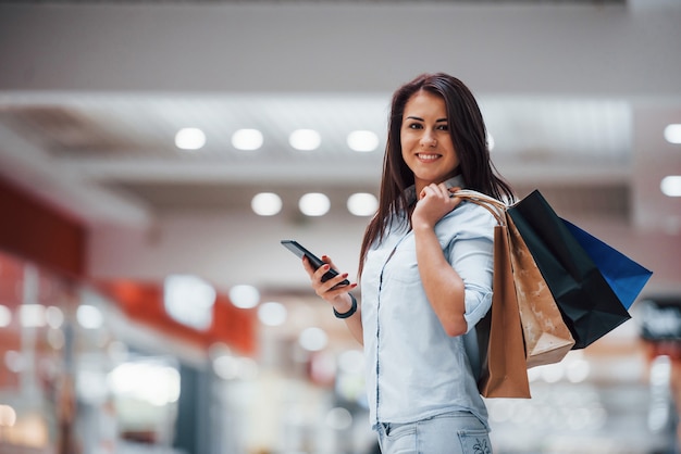 La donna castana al supermercato con molti pacchi e il telefono in mano ha una giornata di shopping.