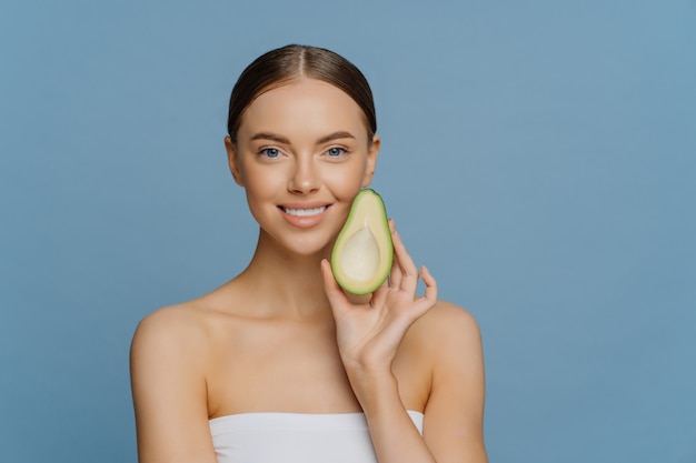 La donna castana felice tiene metà dell'avocado vicino al viso