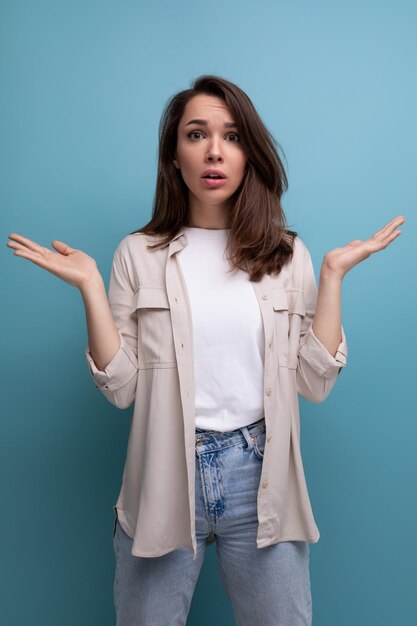 La donna castana sorpresa vestita con una camicia alza le mani