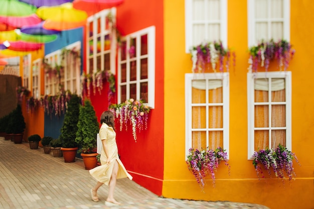 La donna castana turistica di viaggio in vestito giallo cammina per le strade con decorazioni luminose della città. Sfocatura dell'obiettivo decentrabile