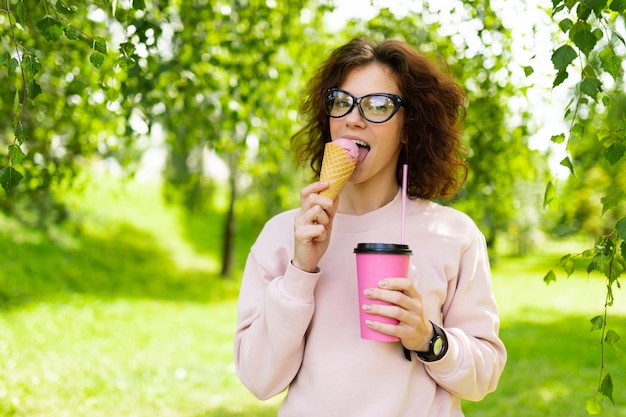 La donna caucasica abbastanza giovane va a fare una passeggiata al parco con caffè e gelato