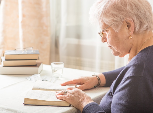 La donna caucasica anziana legge un libro. Rilassamento del pensionato e concetto di piacere dell'educazione del cervello. Avvicinamento.