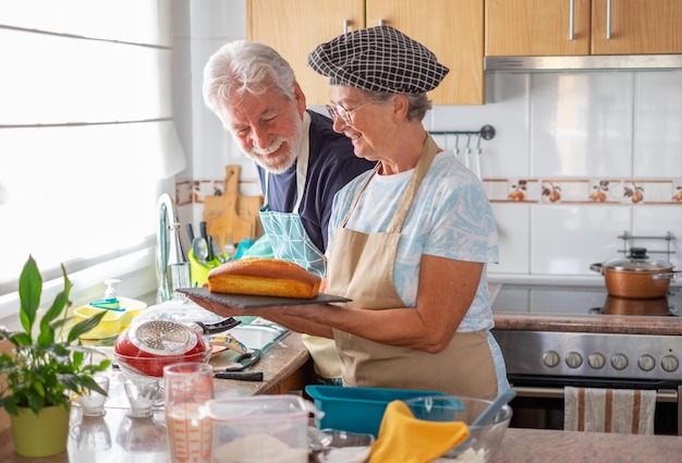 La donna caucasica anziana nella cucina di casa mostra con orgoglio un plumcake fatto in casa appena sfornato al marito