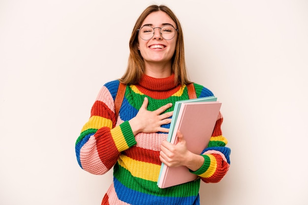 La donna caucasica del giovane studente isolata su fondo bianco ride ad alta voce tenendo la mano sul petto