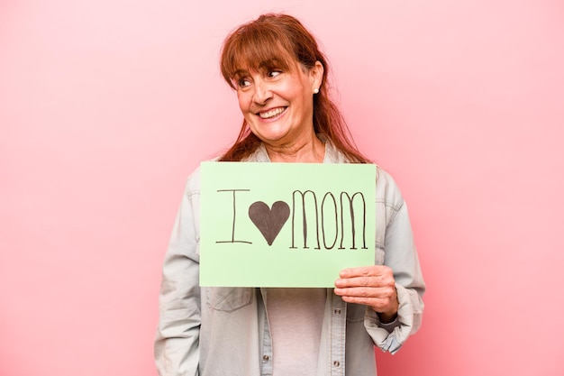 La donna caucasica di mezza età che tiene il cartello I love mom isolato su sfondo rosa sembra da parte sorridente allegro e piacevole