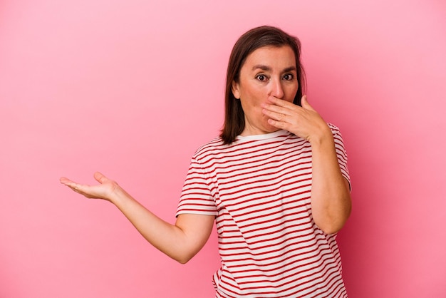 La donna caucasica di mezza età isolata su sfondo rosa ha impressionato tenendo lo spazio della copia sul palmo.