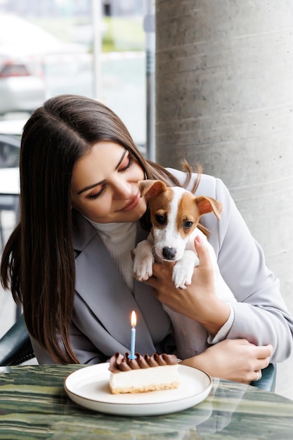 La donna caucasica e il jack russell terrier guardano la torta con una candela festeggiano il compleanno