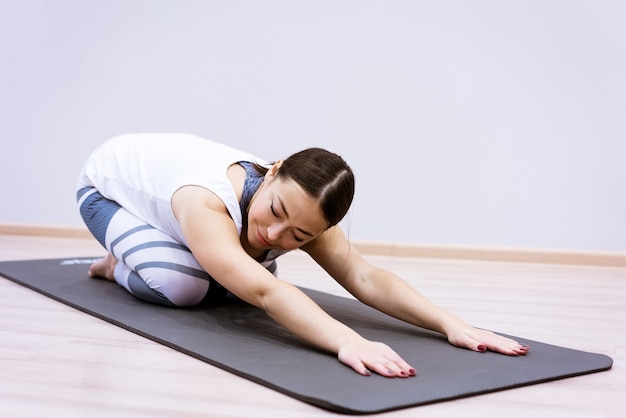 La donna caucasica felice in abiti sportivi pratica lo yoga a casa