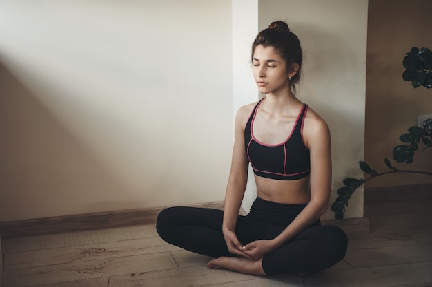 La donna caucasica in abbigliamento sportivo sta meditando sul pavimento mentre fa esercizi di ginnastica a casa
